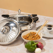 3.5 liter Stainless steel Pressure Cooker set with strainer and Lid along with a bowl of noodles and vegetables on a marble surface.