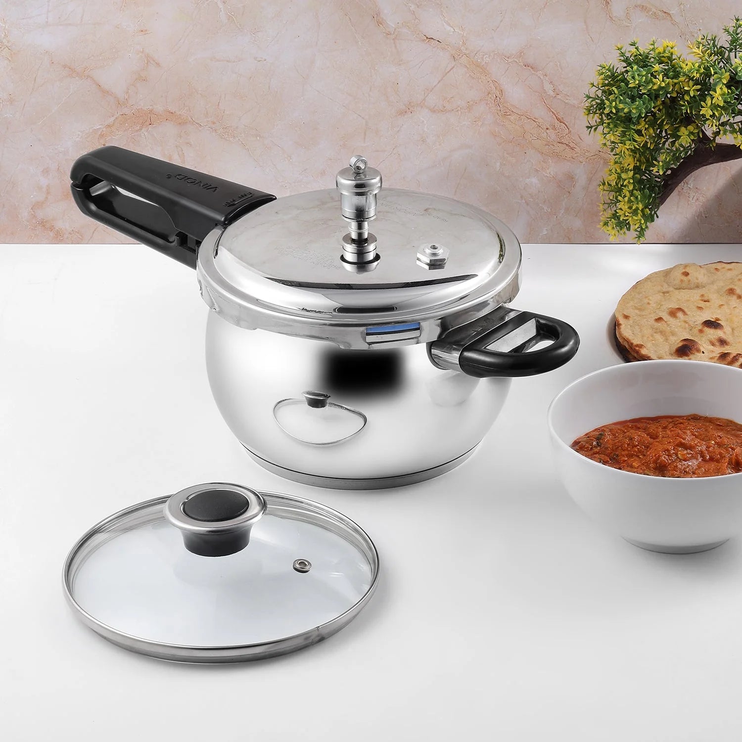 Stainless steel pressure cooker with a glass lid on a marble countertop.