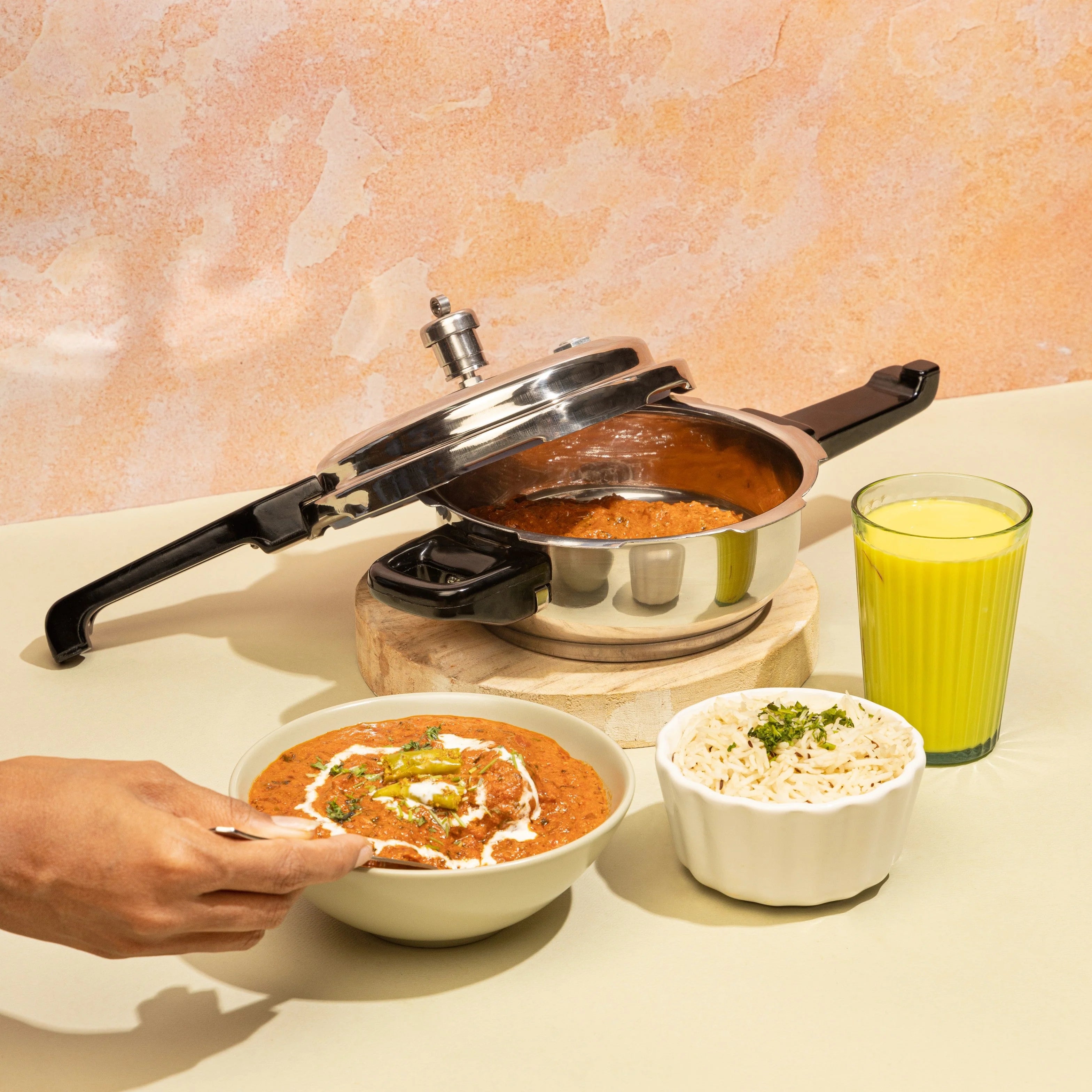 Pressure cooker with food, a bowl of curry, a bowl of rice, and a glass of juice on a table.