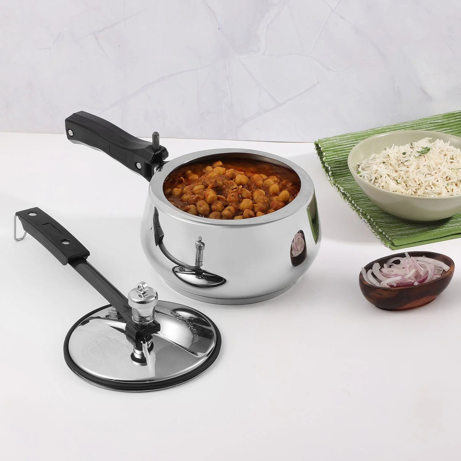 Pressure cooker with a lid on a white surface, surrounded by bowls of food.
