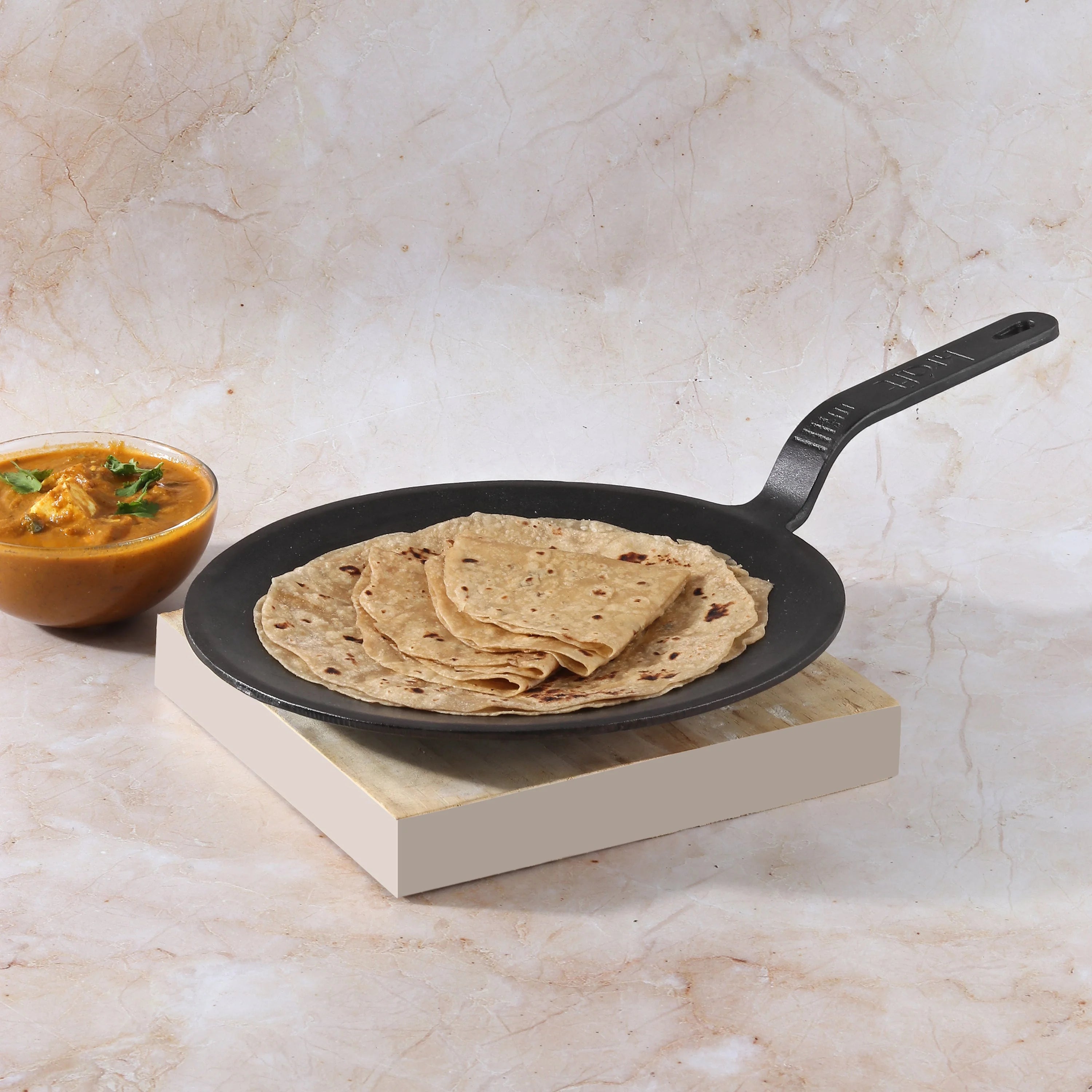 Handcrafted Kraft traditional cast iron cookware with roti on a wooden base.
