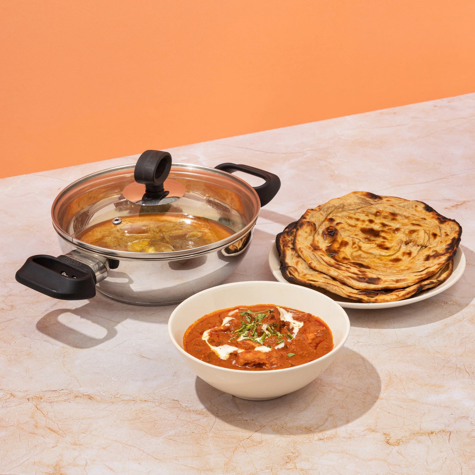 Vinod Deluxe stainless steel kadai used for cooking Indian cuisine, featuring butter chicken and paratha, perfect for flavorful meals
