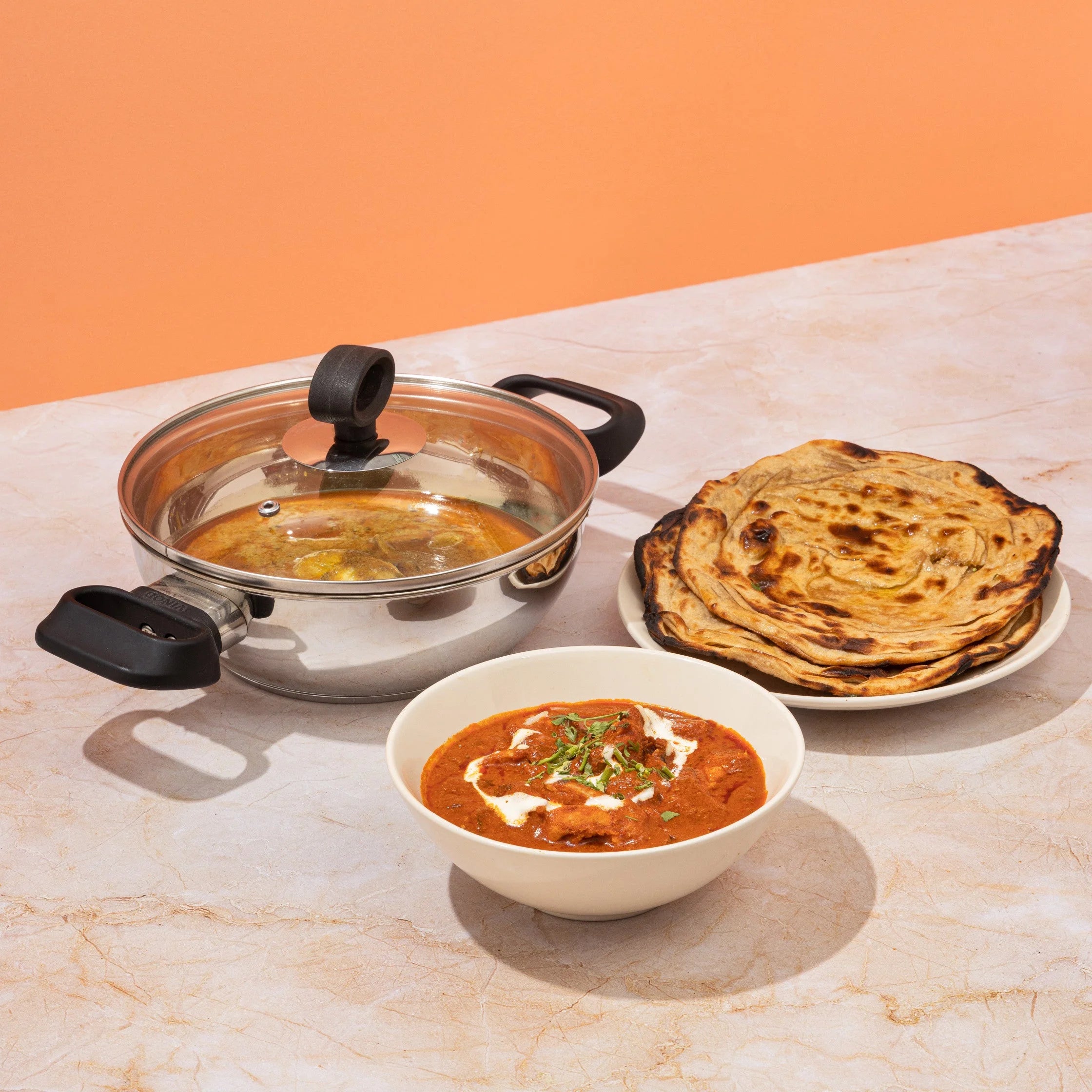 Vinod Deluxe stainless steel kadai used for cooking Indian cuisine, featuring butter chicken and paratha, perfect for flavorful meals