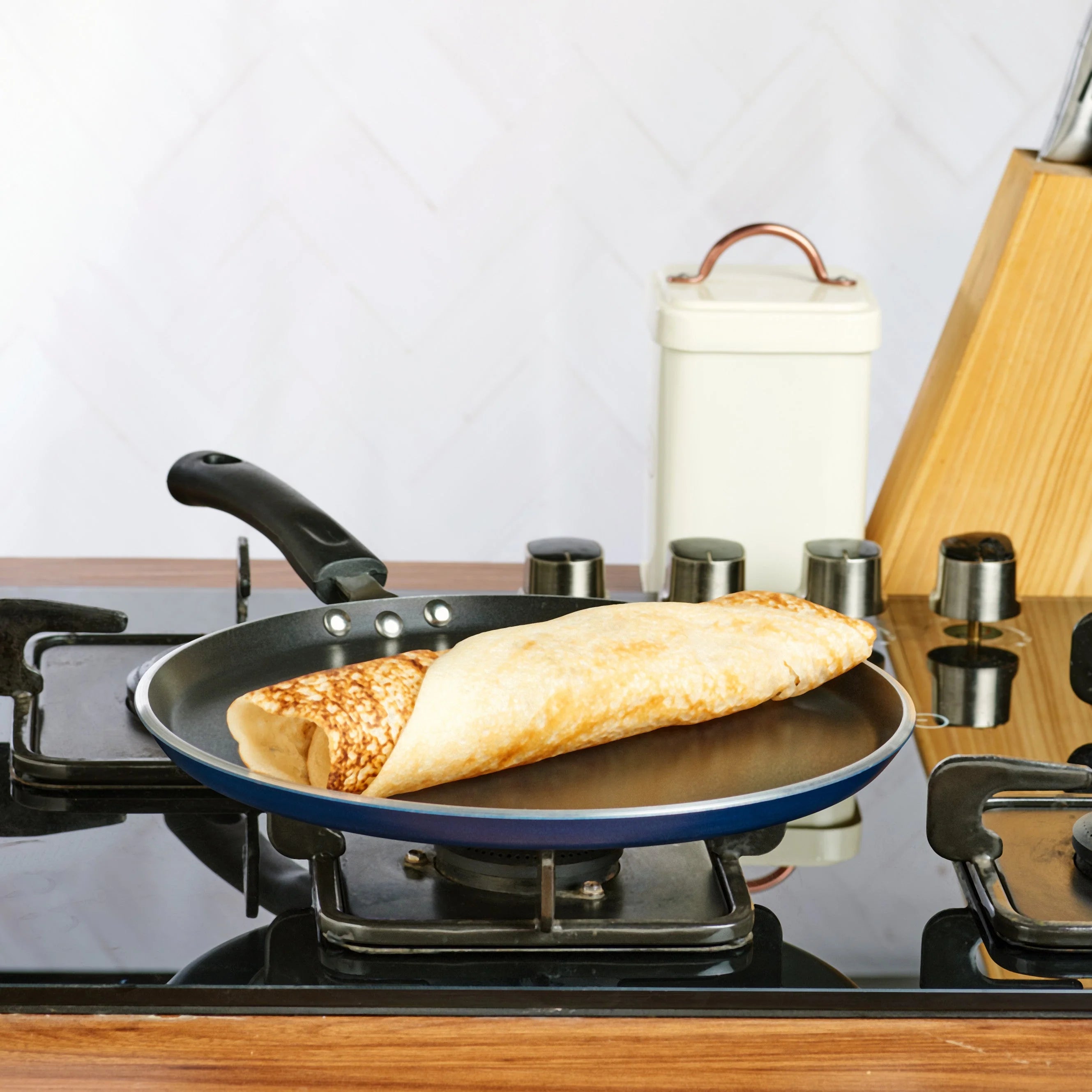 dosa being cooked in a vinod omni 28cm tawa on a gas stove with a kitchen background