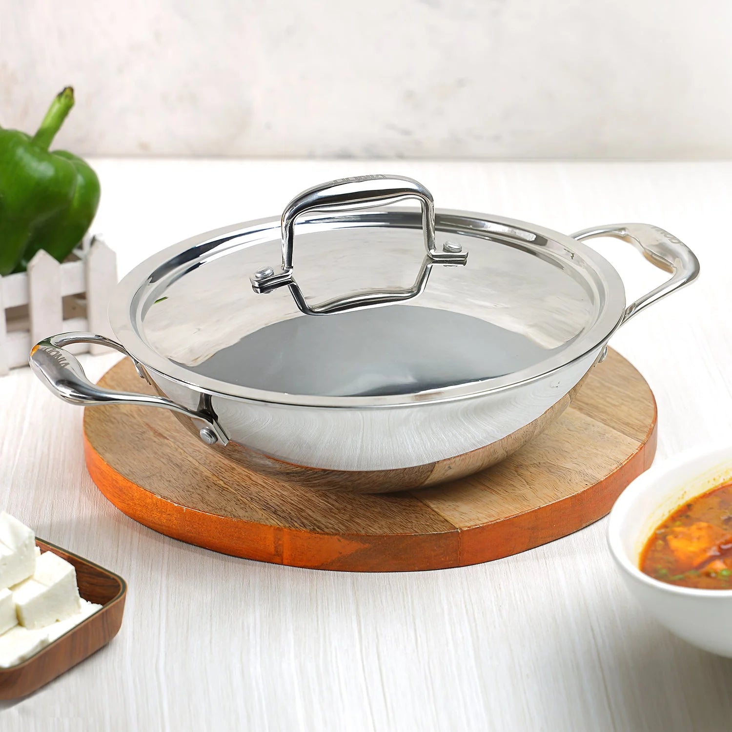 Vinod Platinum triply stainless steel kadai with glass lid on wooden cutting board in modern kitchen setting demonstrating elegant design and functionality
